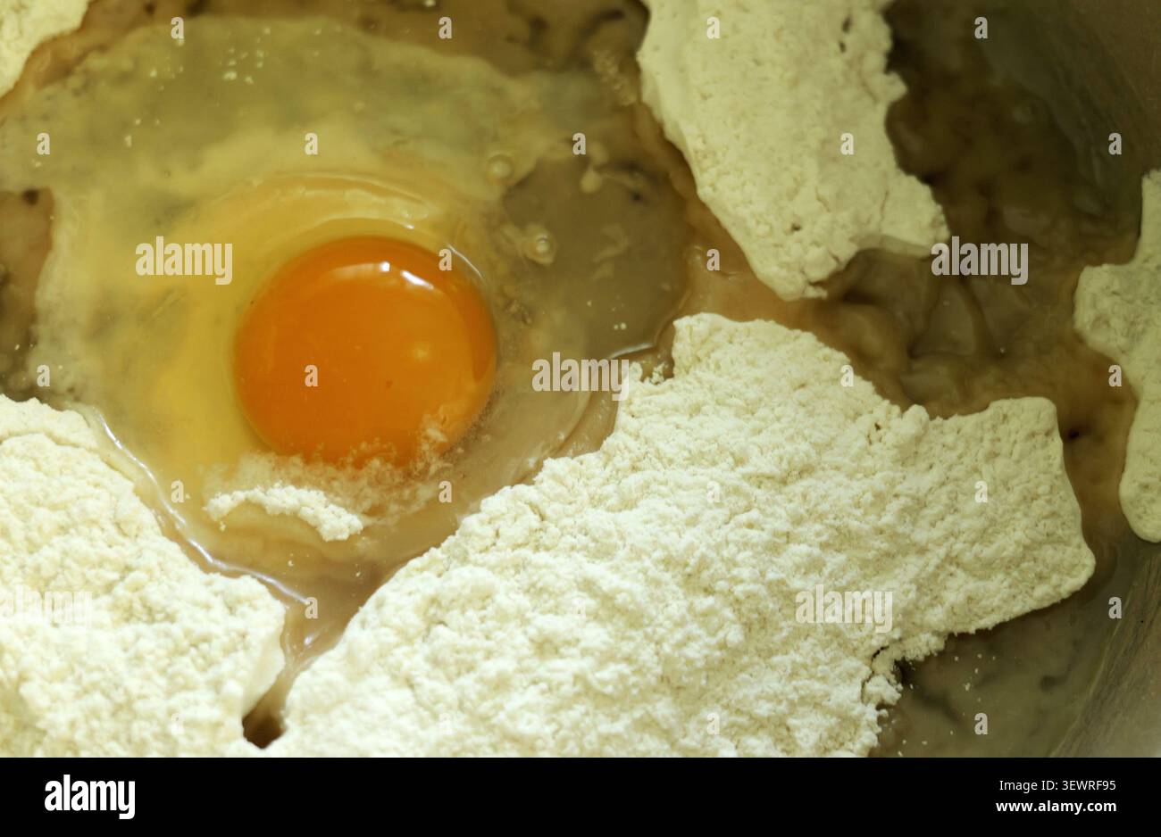 Jaune d'oeuf frais et blanc se fondant dans un tas de farine blanche, mélangeant les ingrédients pour créer un mélange de pâte parfait pour la cuisson, la cuisson ou la pâtisserie Banque D'Images