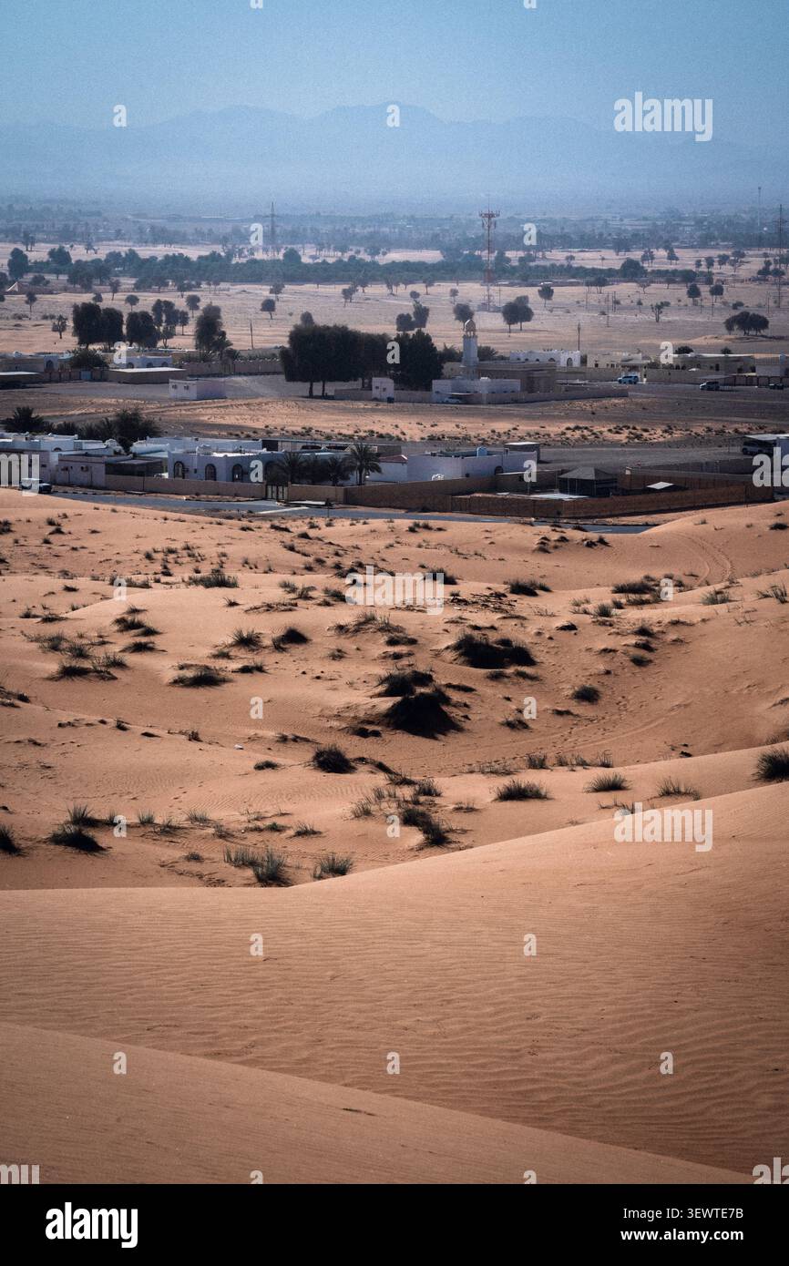 Vue de Fossil Rock s'élevant au-dessus des vastes dunes de sable du désert de Mleiha, avec une petite colonie et une mosquée visibles au loin, Mleiha, Sharjah Banque D'Images
