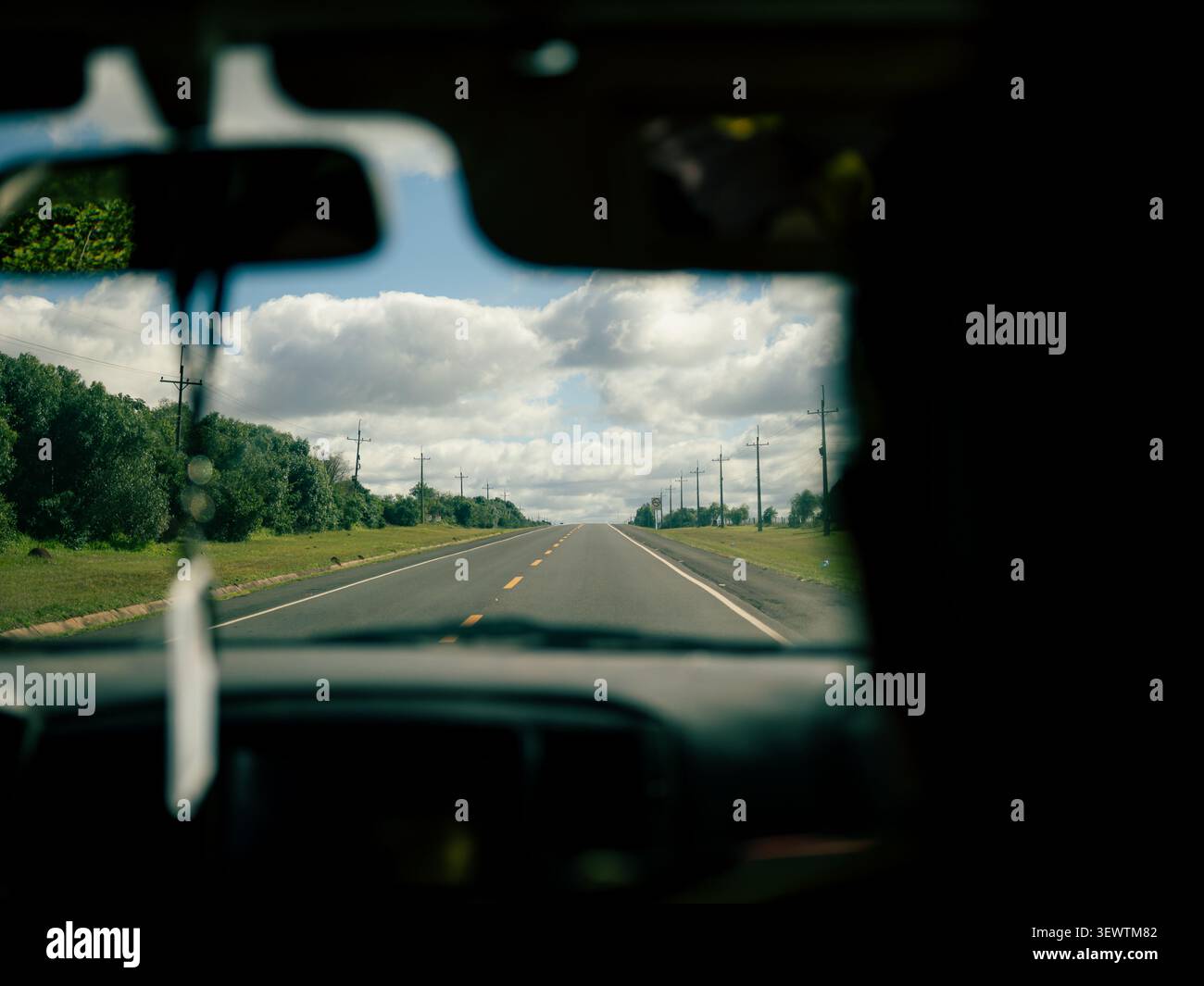 À l'intérieur d'une voiture, le pare-brise encadre la vue. Une route droite s'étend devant vous sous un ciel nuageux. Des arbres verts bordent les côtés de la route. Lignes électriques point th Banque D'Images