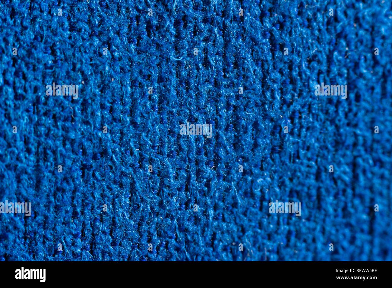 Un tissu tricoté bleu profond remplit le cadre. La texture montre des rangées de points entrelacés. Une vue rapprochée met en évidence les détails fins du fil. Couleur douce et uniforme Banque D'Images