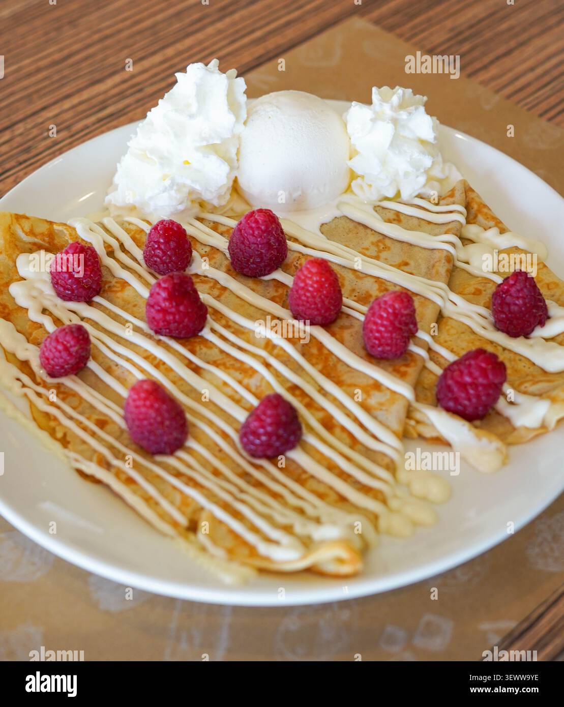 Crêpes au filet de chocolat blanc, framboises, crème fouettée et glace à la vanille sur une assiette blanche Banque D'Images