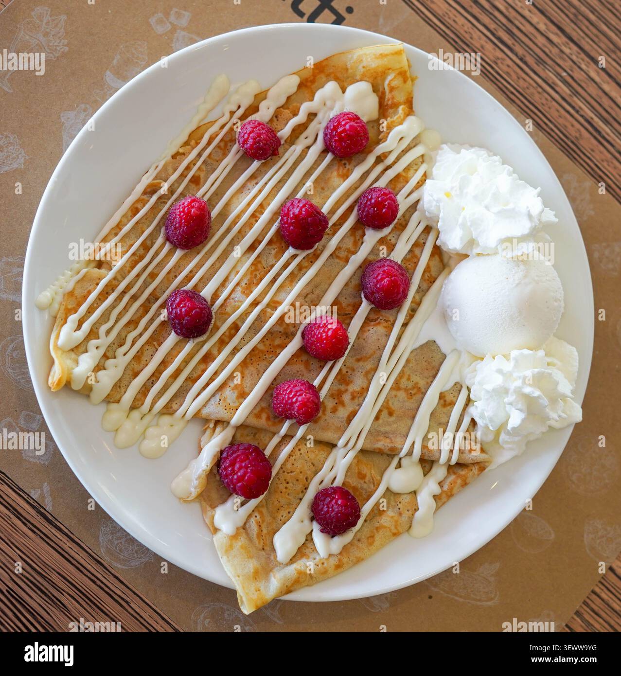 Crêpes au filet de chocolat blanc, framboises, crème fouettée et glace à la vanille sur une assiette blanche Banque D'Images