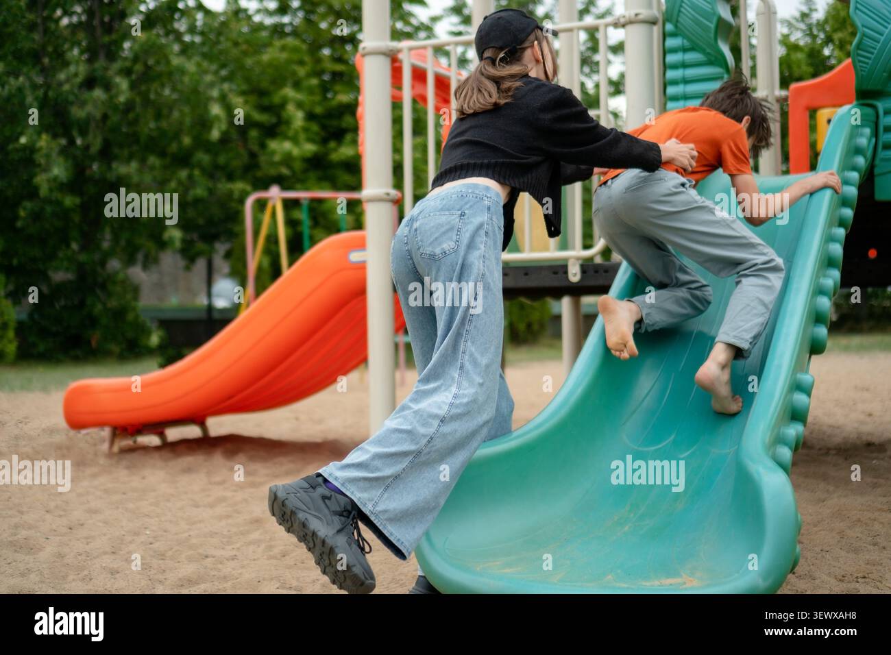 Un enfant joyeux et un frère adolescent glissent ensemble sur un terrain de jeu bleu. Des frères et sœurs insouciants partagent une promenade passionnante dans le parc. Frère et sœur profitent d’un moment ludique et amusant sur le sable Banque D'Images