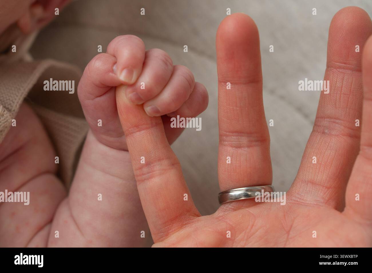 Une photo conceptuelle réconfortante montrant la différence de taille entre la main d'un parent avec une bague de mariage et le petit poing d'un nouveau-né. Concept de Banque D'Images