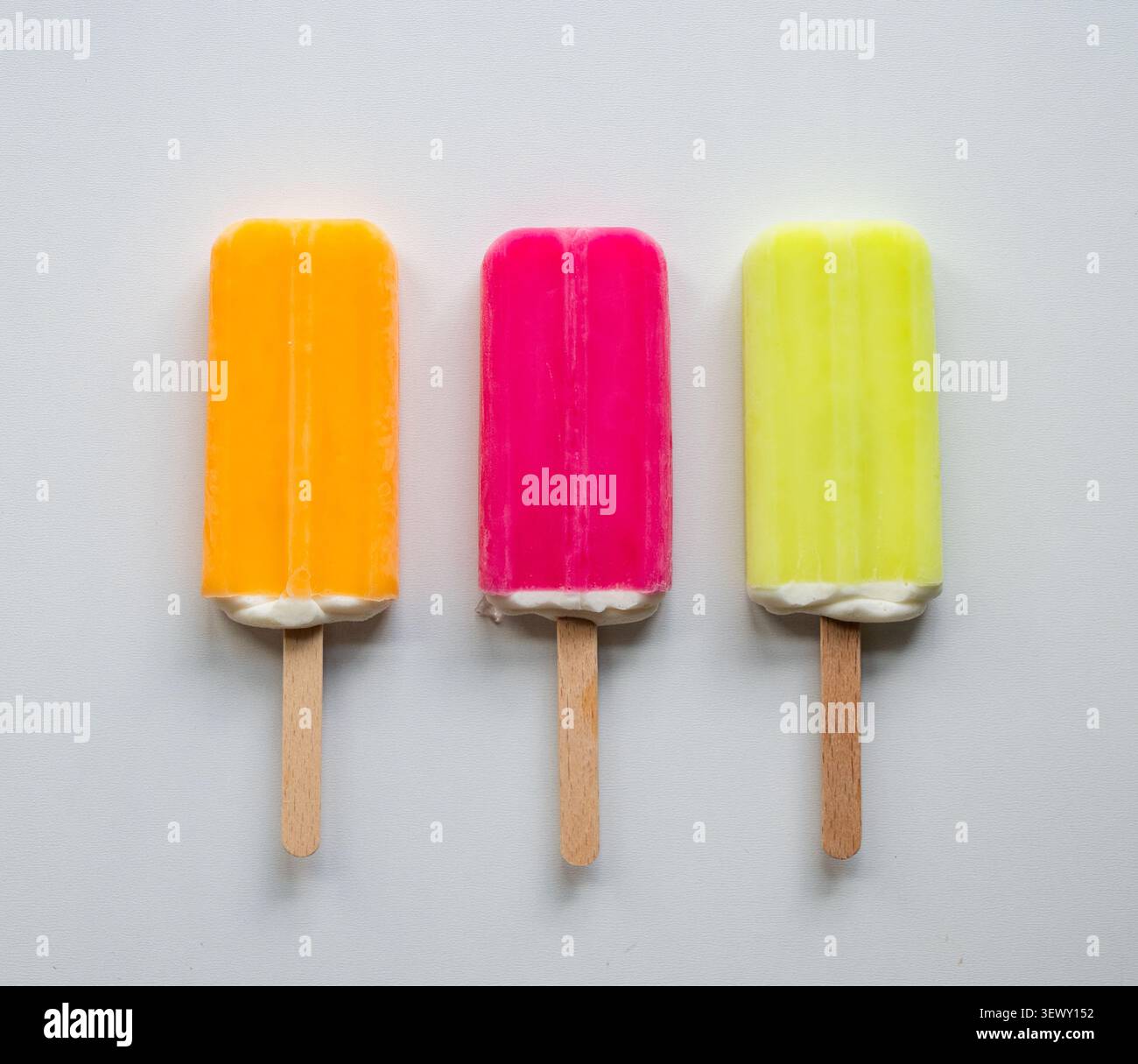 Trois popsicles colorées vives dans une rangée sur fond blanc. Banque D'Images
