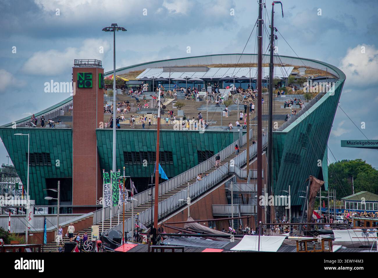 3 août 2024, Amsterdam, pays-Bas : les visiteurs se rassemblent sur le toit-terrasse du musée des sciences NEMO surplombant le port par une journée nuageuse d'été. Banque D'Images