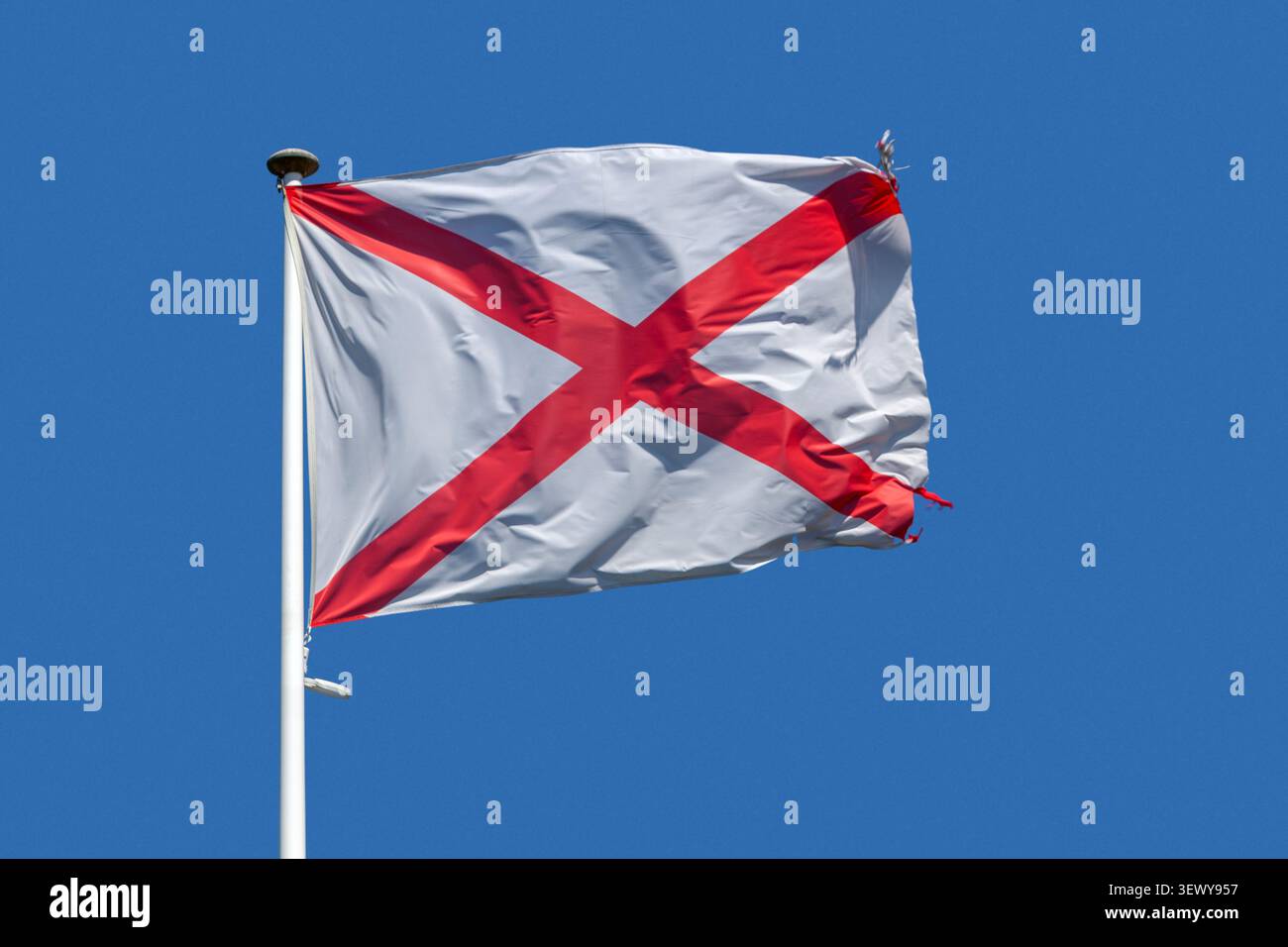 Rouge : Croix d'Andrew (saltire) sur un champ blanc ondulant au sommet de son poteau contre un ciel bleu. C'est le drapeau officiel de l'Alabama. Banque D'Images