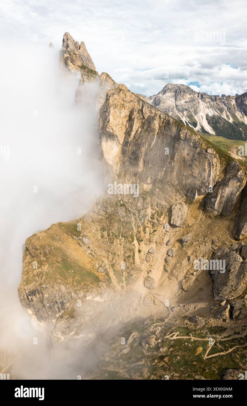 Drone spectaculaire vue aérienne falaises rocheuses déchiquetées ligne de crête Seceda partiellement couverte de nuages blancs ondulants commuchback randonnée sentier vallée paysage alpin donc Banque D'Images