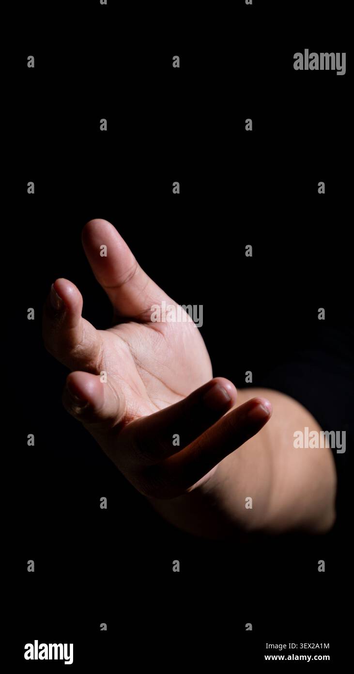 Image discrète d'une main ouverte étendue vers l'avant, éclairée par un faisceau de lumière étroit. La pose transmet à nouveau l'offrande, l'expression et la profondeur émotionnelle Banque D'Images