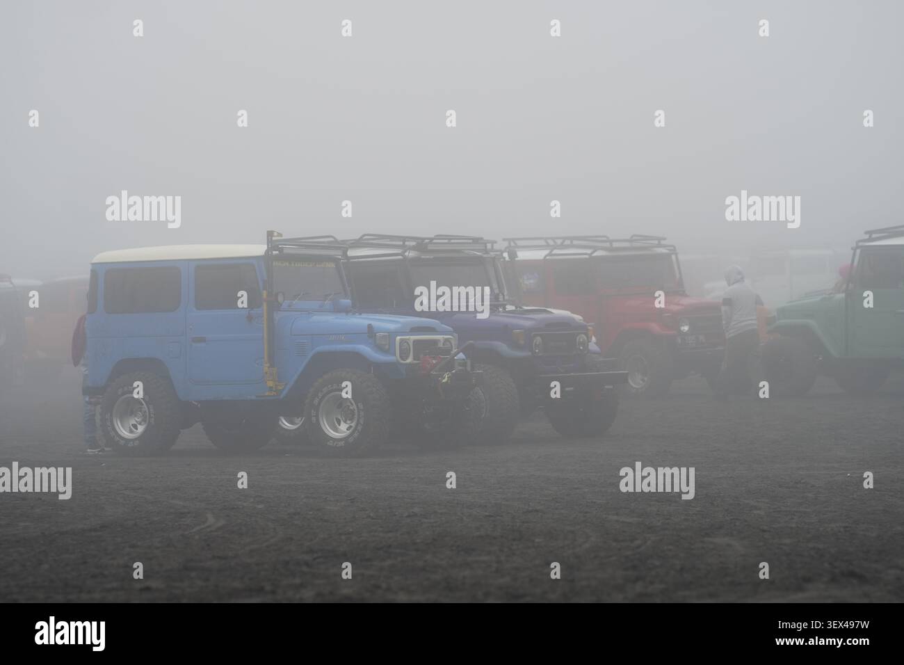 Voitures jeep 4x4 hors route colorées classiques garées sur une mer de sable volcanique sous une épaisse brume épaisse et de brouillard au mont bromo, Java oriental, Indonésie. Banque D'Images
