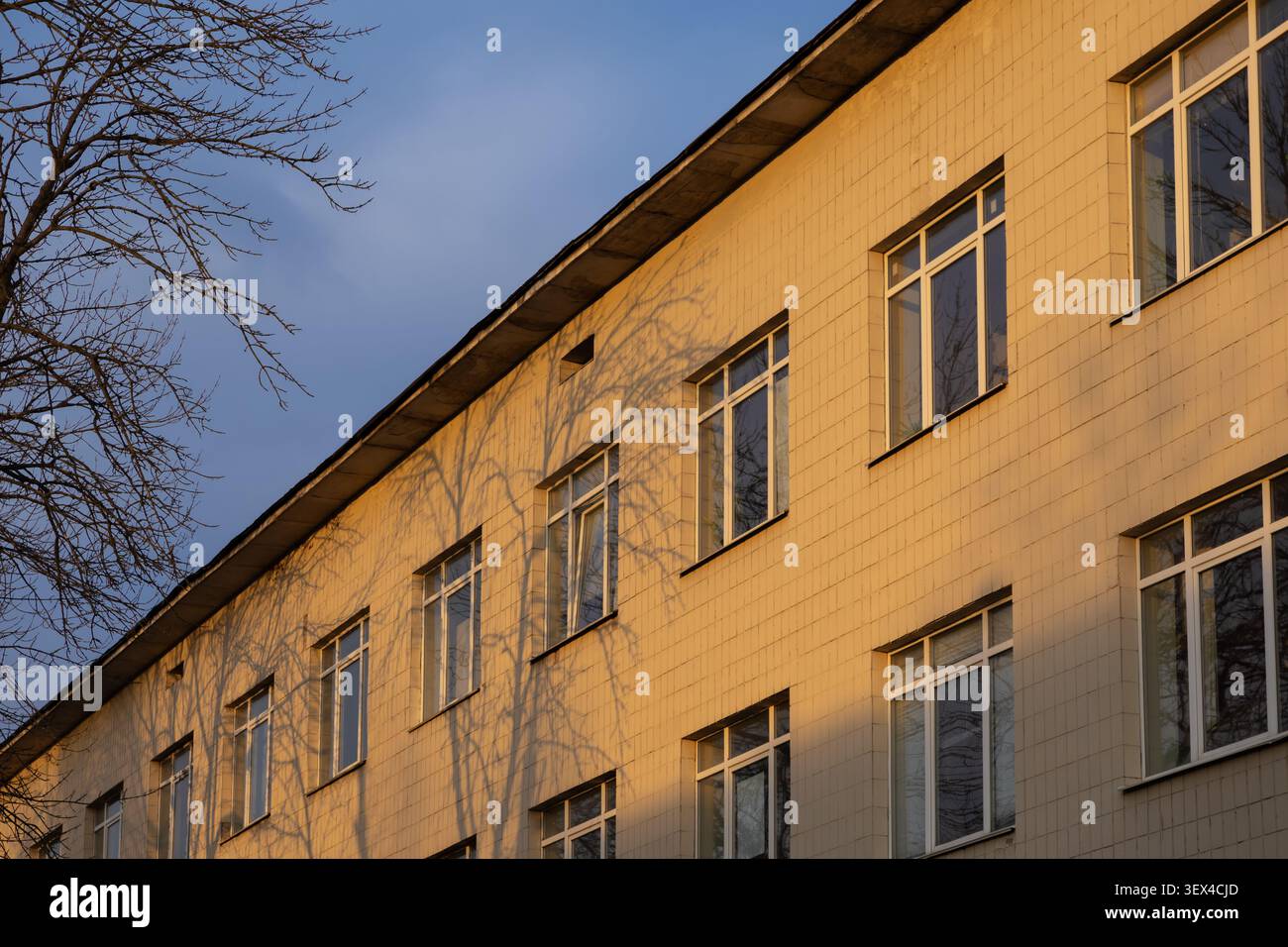 Cette façade texturée d'un bâtiment de bureau ou d'école présente des rangées uniformes de fenêtres, capturées pendant le coucher du soleil pour souligner la lumière chaude, les ombres profondes, a Banque D'Images