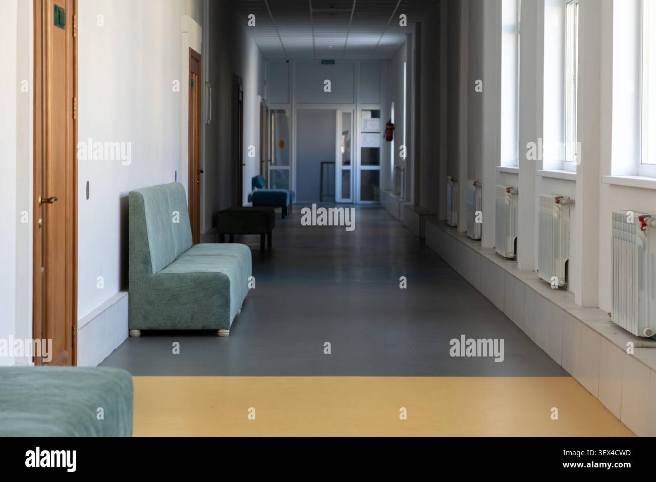 Long couloir dans un immeuble de bureaux contemporain avec des sièges doux pour les visiteurs, où la lumière vive et les tons discrets transmettent un sentiment de calme Banque D'Images
