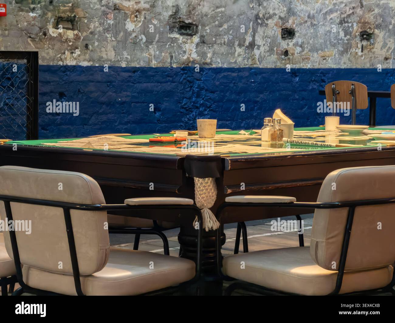 Cette table de billard réaménagée est transformée en salle à manger commune dans un lieu industriel avec des murs texturés et un satin confortable Banque D'Images