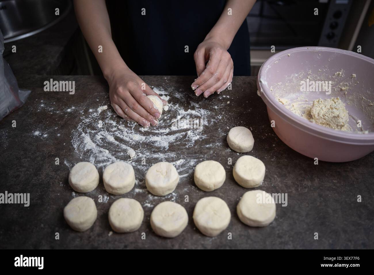 Les mains de la personne façonnent soigneusement et répartissent la pâte en petits morceaux circulaires sur un comptoir de cuisine saupoudré de farine, préparant les ingrédients pour la cuisson Banque D'Images