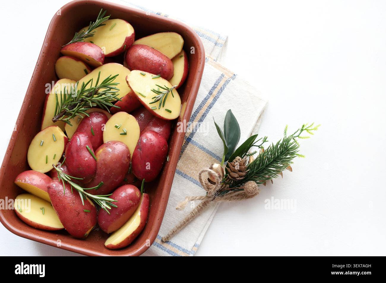 Plan en contre-plongée de pommes de terre à peau rouge tranchées assaisonnées de brins de romarin dans un plateau en céramique. Plat végétalien sain, mise en scène rustique. Banque D'Images