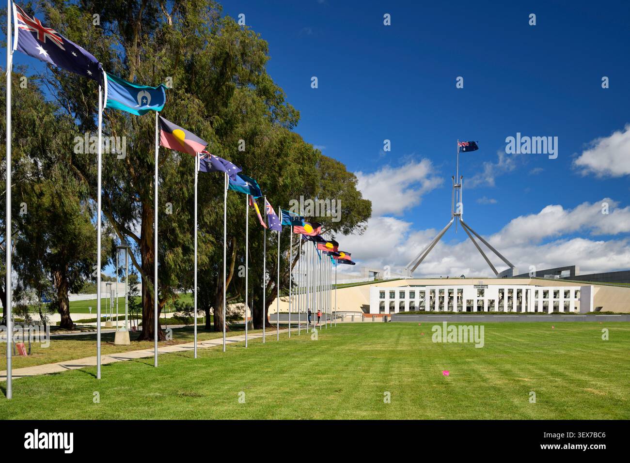 Australie, territoire de la capitale australienne, Canberra, Parlement, façade principale et mât de drapeau de 81 mètres arborant le drapeau australien, vu de la pelouse de cérémonie bordée de drapeaux australiens, aborigènes et insulaires du détroit de Torres Banque D'Images