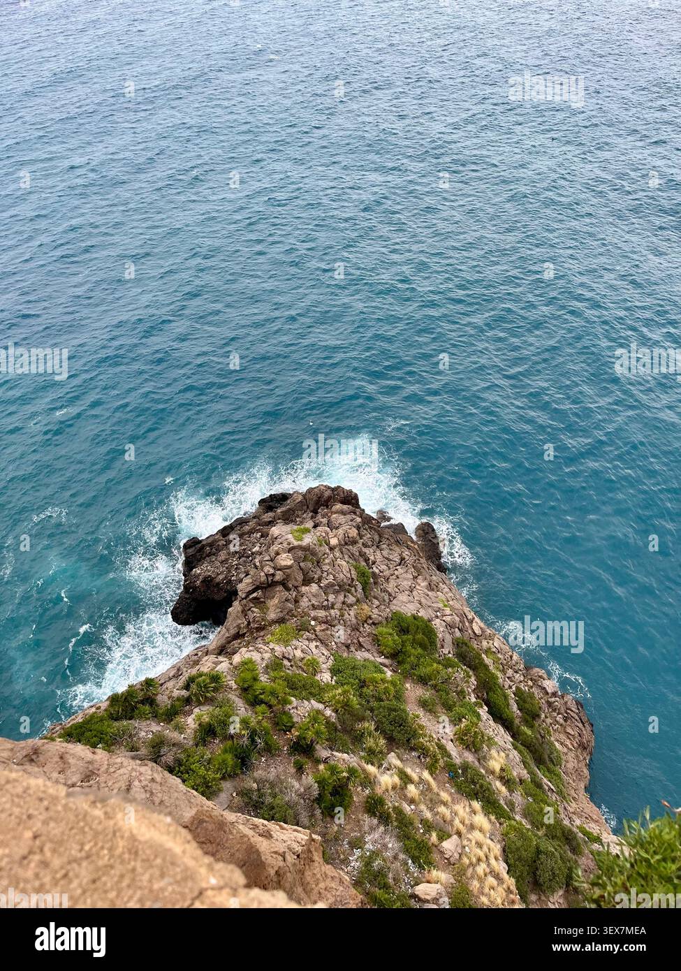Vue en haut angle d'une falaise rocheuse avec une végétation verte rencontrant les vagues écrasantes de la mer Méditerranée bleue à Bejaia, Algérie - Image de stock capturée avec un smartphone