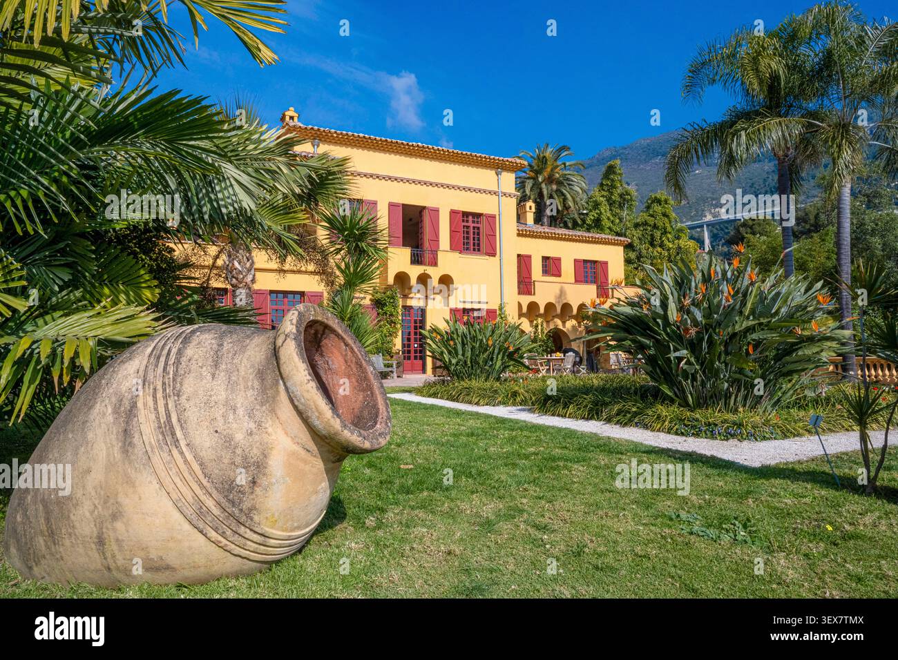 France, Alpes Maritimes, Côte d'Azur, Menton, jardin botanique de Val Rahmeh, amphore géante dans le jardin botanique de Val Rahmeh, la villa jaune ocre d'inspiration provençale italienne avec oiseau du Paradis (Strelitzia reginae) au premier plan Banque D'Images