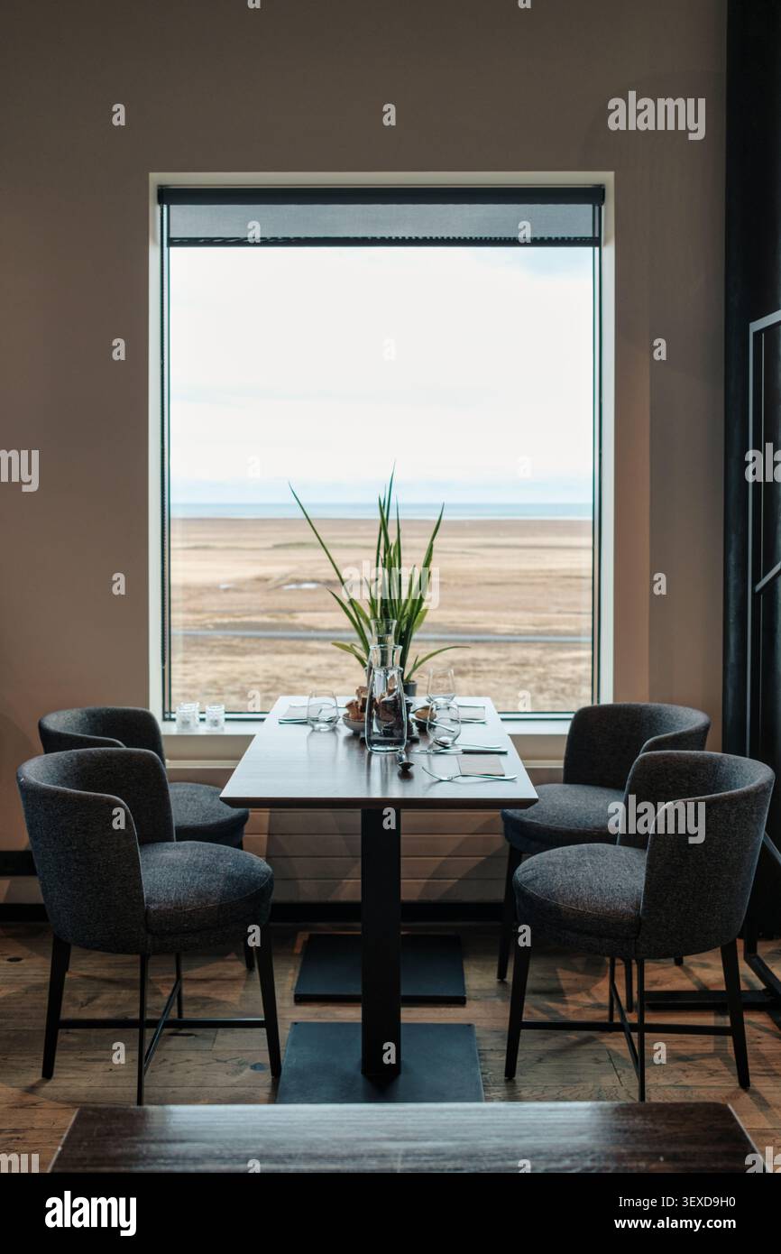 Élégante table à manger dans le restaurant scandinave, à côté d'une grande fenêtre donnant sur un champ désertique serein et décor minimaliste Banque D'Images