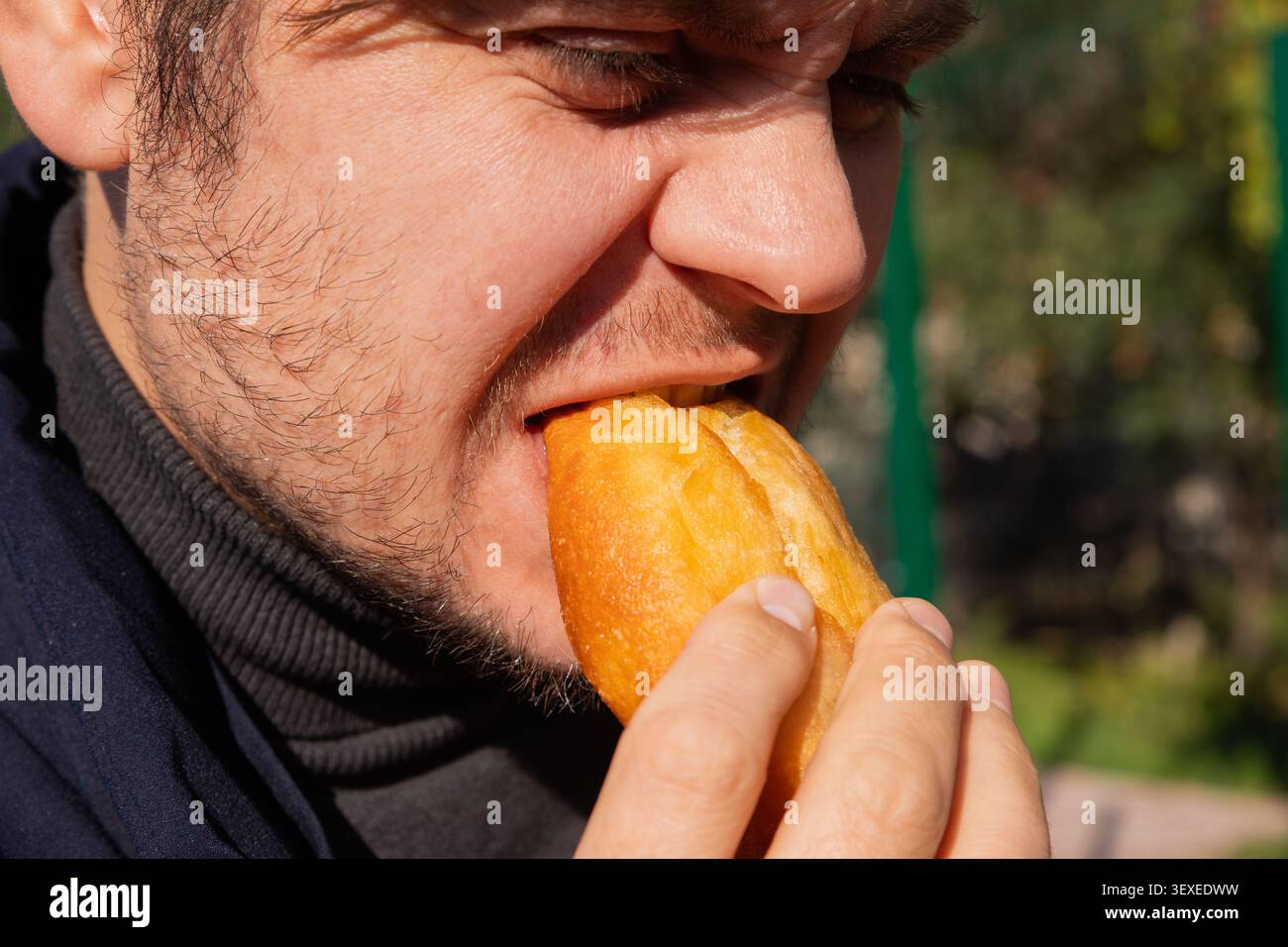 Homme mangeant de la pâtisserie frite avec garniture de pommes de terre. Un type caucasien qui a une collation rapide de la nourriture de rue à l'extérieur. Délicieux pain à la pâte dorée avec farce de légumes Banque D'Images