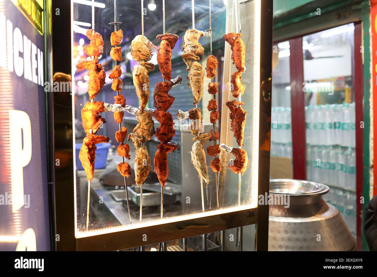 Poulet fraîchement grillé, poulet tikka et barbecue de style tandoori présentés sur des brochettes métalliques dans une vitrine de restaurant le soir. Banque D'Images