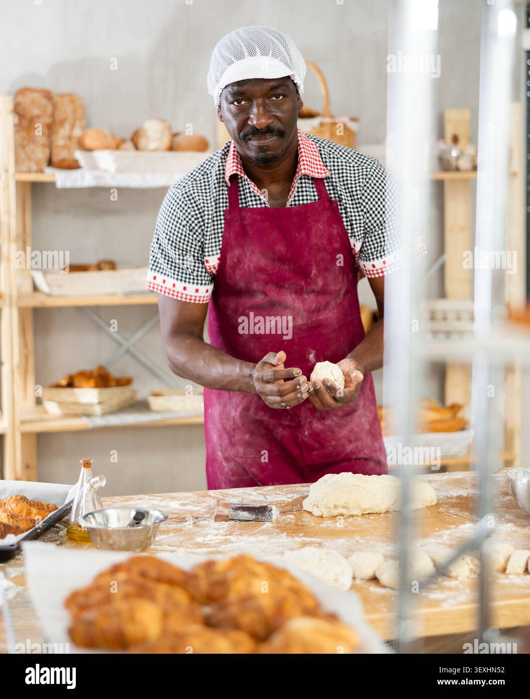 Boulanger professionnel travaillant avec des morceaux de pâte sur la table farinée Banque D'Images