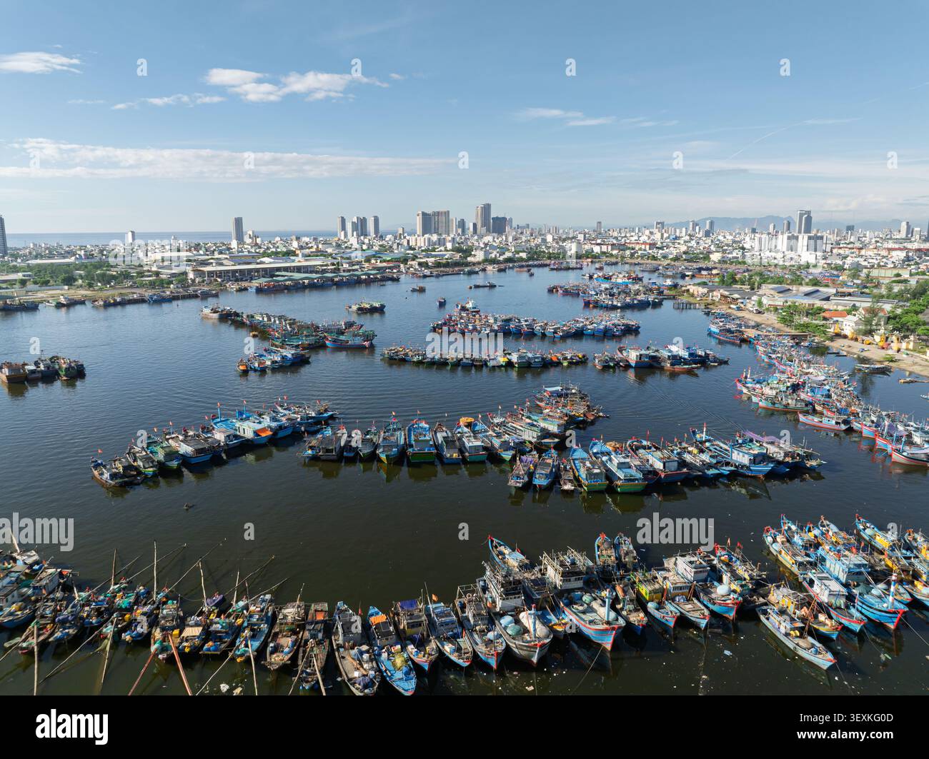 Vue aérienne de bateaux de pêche colorés ancrés dans la baie de Da Nang, Da Nang, Vietnam, avec une ligne d'horizon moderne sous un ciel bleu clair. Banque D'Images