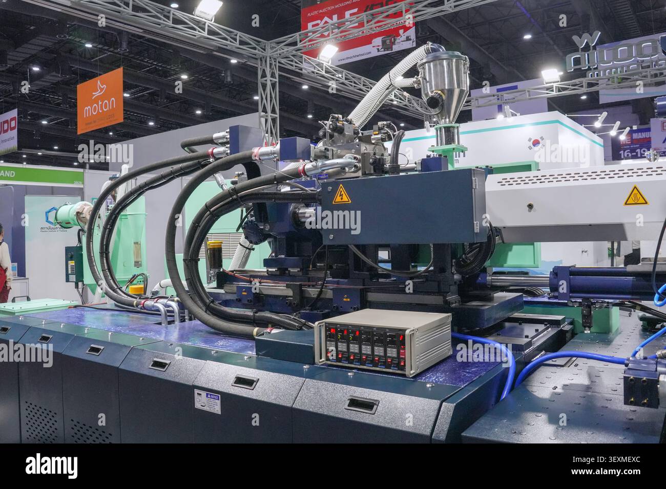 Bangkok, Thaïlande - 17 juin 2026 : machine de moulage par injection bleue avec tuyaux hydrauliques exposés au hall d'exposition du salon Manufacturing Expo. Banque D'Images