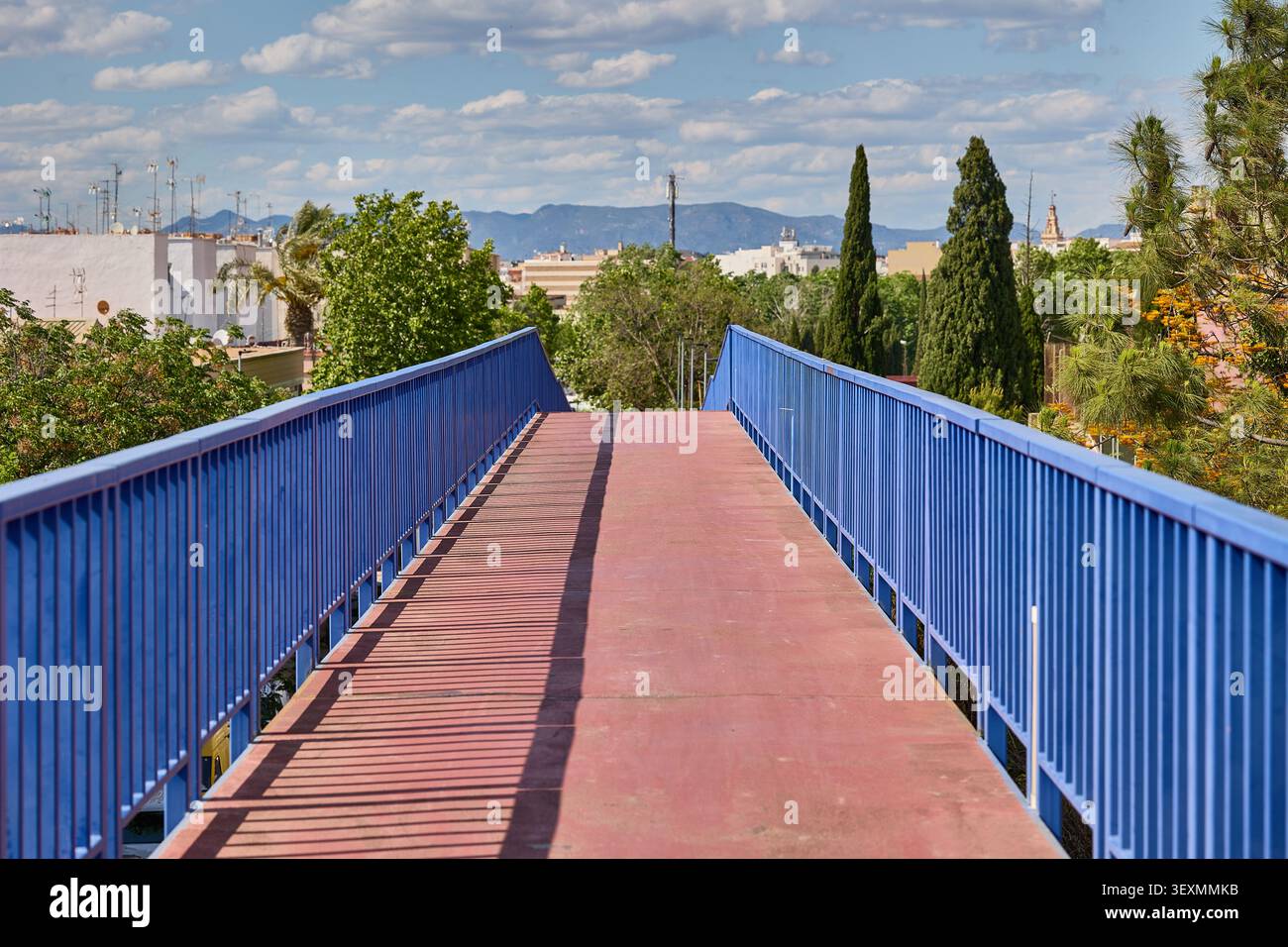 Pont piétonnier rouge avec garde-corps bleus et vue sur la ville de Valence sous le ciel bleu. Banque D'Images
