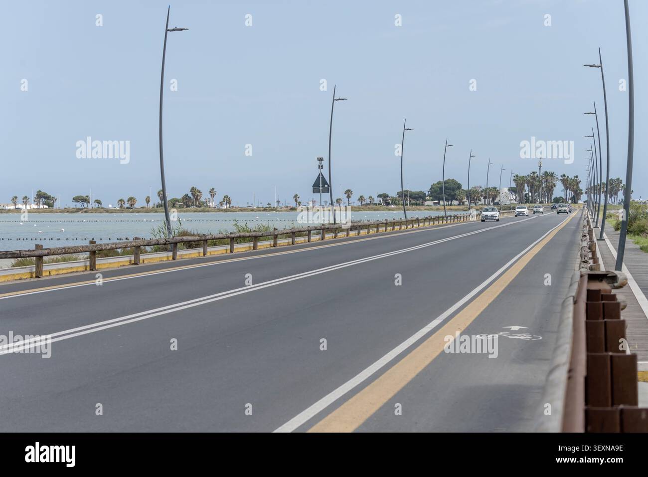 CAGLIARI, 2026 avril 29 ; paysage éditorial avec circulation automobile clairsemée sur le pont traversant la lagune de Montelargius avec des flamants roses dans son eau, tourné en brick Banque D'Images