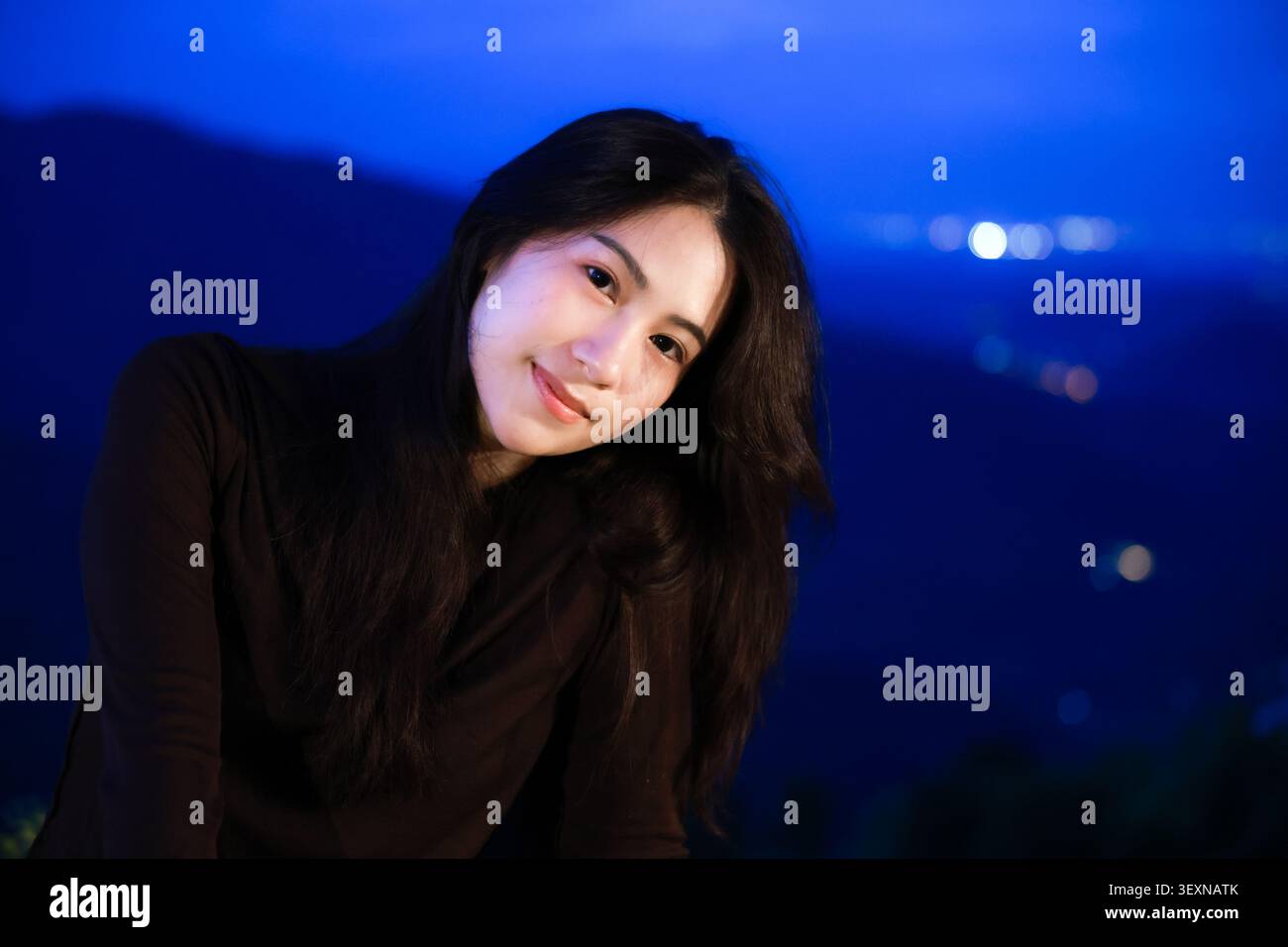 Une jeune femme à cheveux longs chemise noire souriante en plein air nuit bleu montagne fond serein beauté naturelle paisible lumière douce détendue pose bonheur Banque D'Images