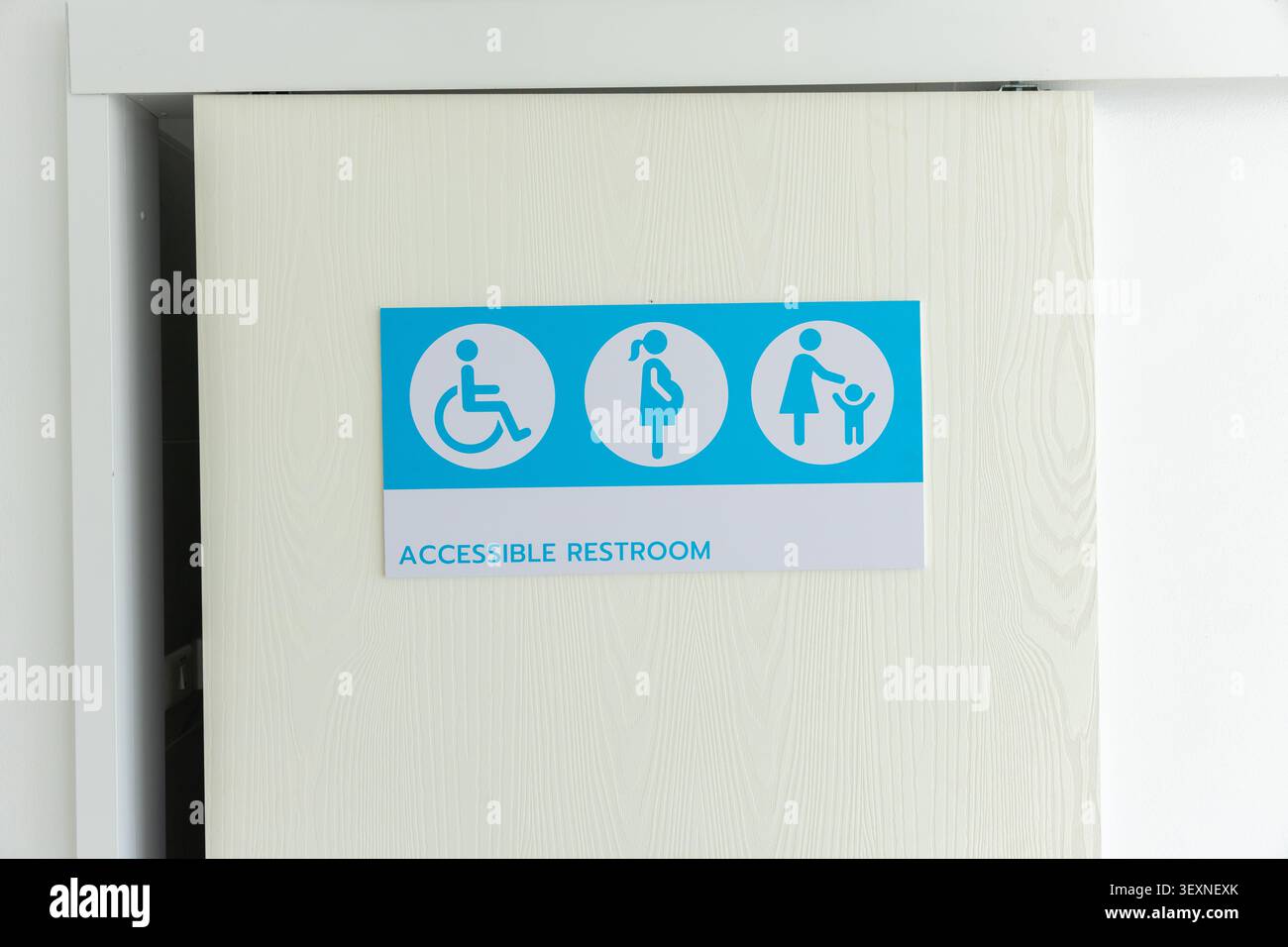Un panneau de toilettes accessibles avec des icônes bleues pour l'utilisateur de fauteuil roulant, la femme enceinte et l'adulte avec enfant sur la porte en bois blanc, indiquant bain inclus Banque D'Images