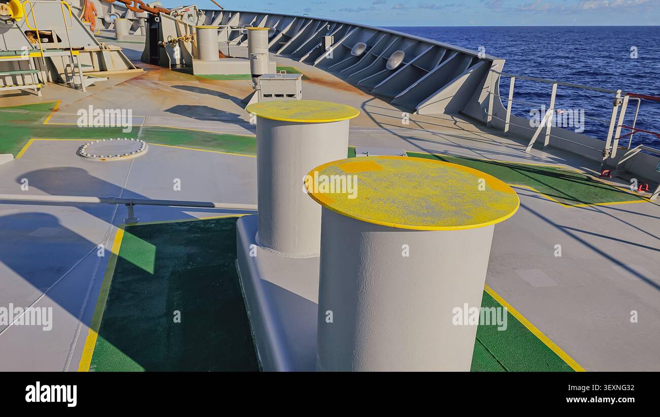 Gros plan horizontal de bittes d'amarrage marines robustes avec des sommets jaunes sur un pont de navire, utilisées pour sécuriser les lignes d'amarrage avec un océan bleu profond dedans Banque D'Images