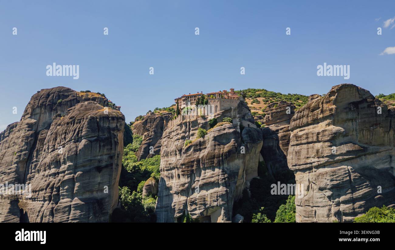 Plan horizontal large drone d'un ancien monastère orthodoxe debout sur une haute falaise parmi les formations rocheuses massives dans les Météores sous un ciel bleu clair i Banque D'Images