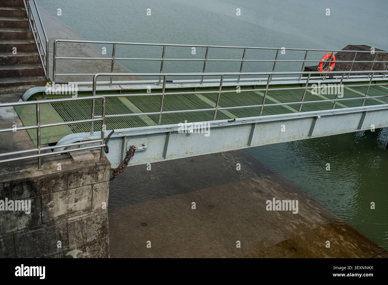 Vue en grand angle d'un pont de passerelle métallique avec terrasse en treillis vert et mains courantes de sécurité s'étendant d'une jetée en béton au-dessus de l'eau. Banque D'Images
