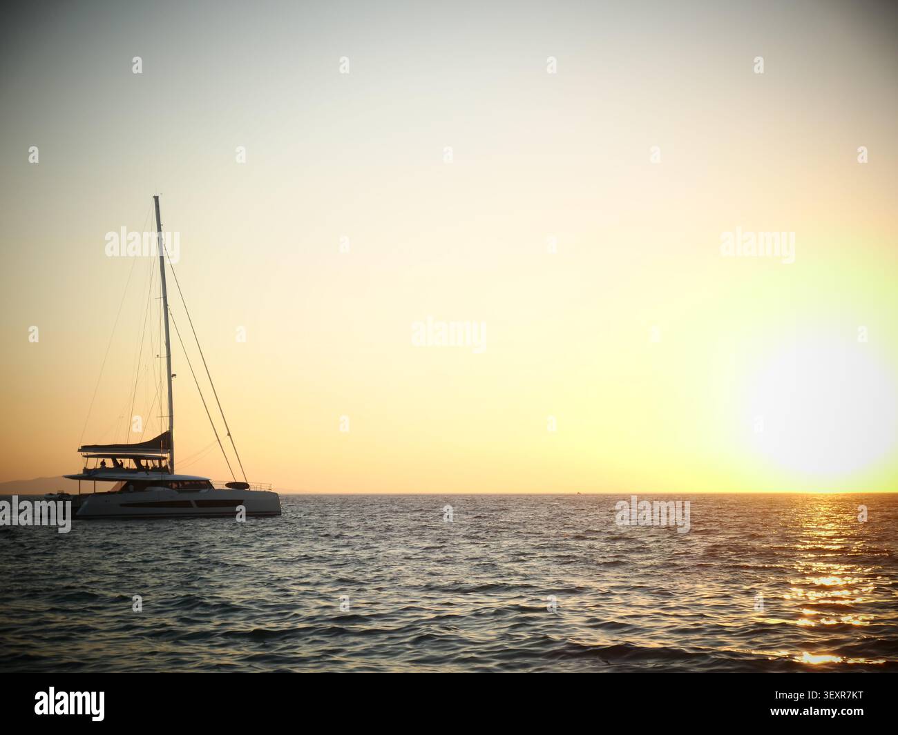 Catamaran silhouette naviguant sur l'océan calme au coucher du soleil Banque D'Images
