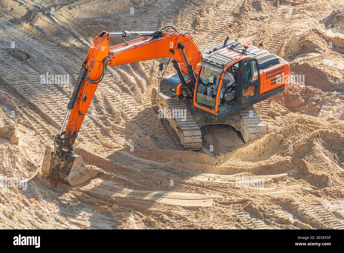 Grande pelle orange travaillant sur terrain sablonneux, bras articulé et godet creusant, conducteur concentré dans la cabine ouverte, chaînes extra-robustes quittant Dee Banque D'Images