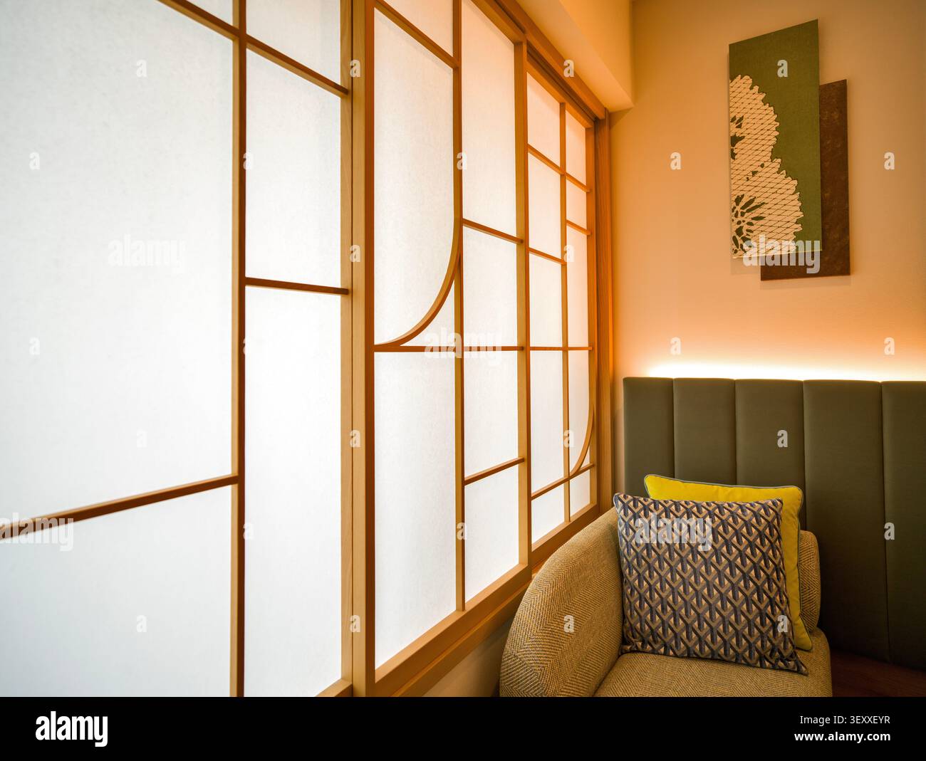 L'intérieur moderne de la chambre d'hôtel japonais comprend une fenêtre incurvée à écran shoji, un canapé confortable, des oreillers à motifs et un éclairage doux et chaleureux. Banque D'Images