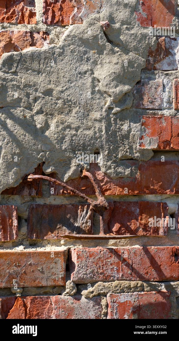 Un vieux mur de briques rouges avec stuc gris fissuré et un élément de barre d'armature en métal rouillé qui dépasse. Banque D'Images