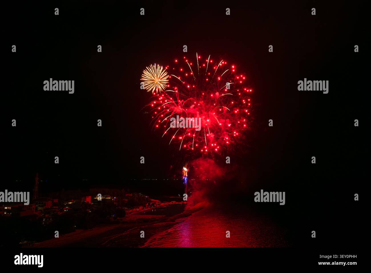 Feux d'artifice nocturne sur le rivage avec éclat rouge et petite floraison dorée Banque D'Images