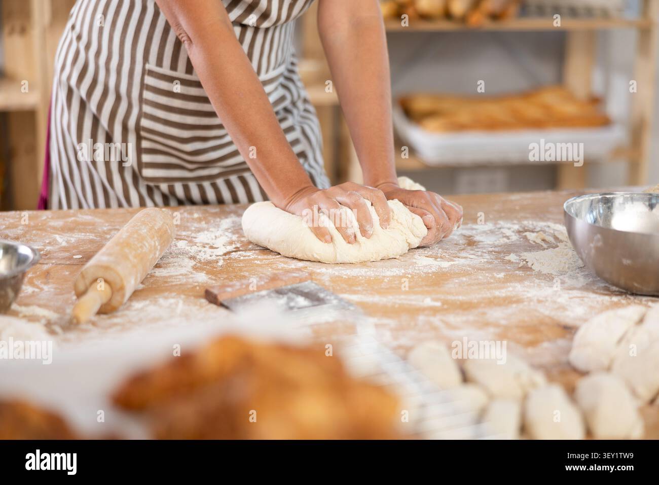 Pâtes mignonnes disposées sur la table dans la boulangerie avec un gros plan des mains féminines pétrissant habilement la pâte à la chaîne de production alimentaire Banque D'Images