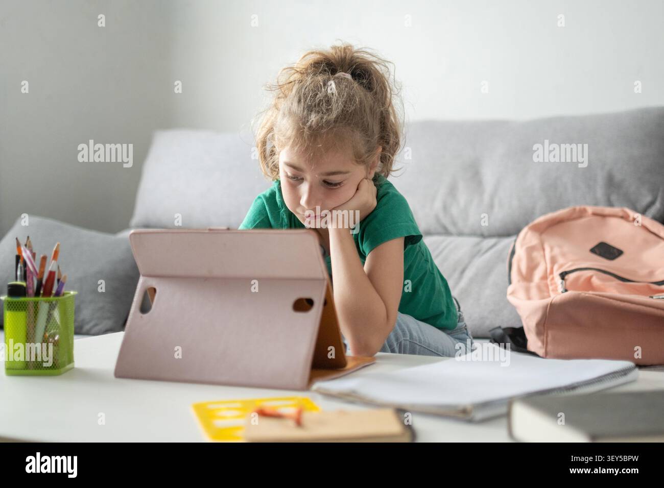 Fille de l'école primaire écrivant des devoirs tout en étant allongée sur le plancher du salon à la maison Banque D'Images