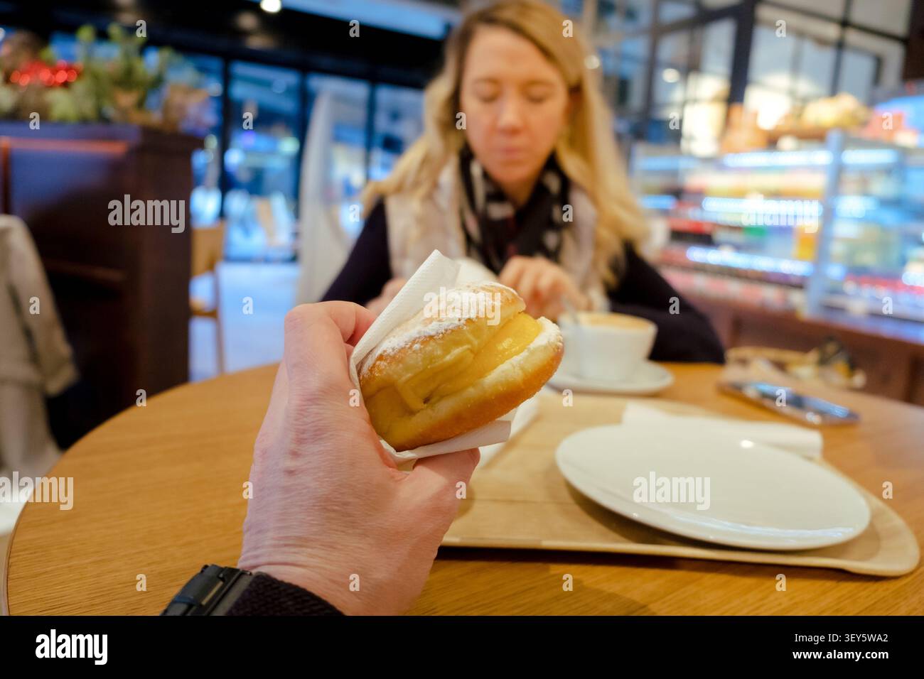 Personne tenant un krapfen avec du sucre en poudre tout en dînant dans un café de boulangerie Banque D'Images