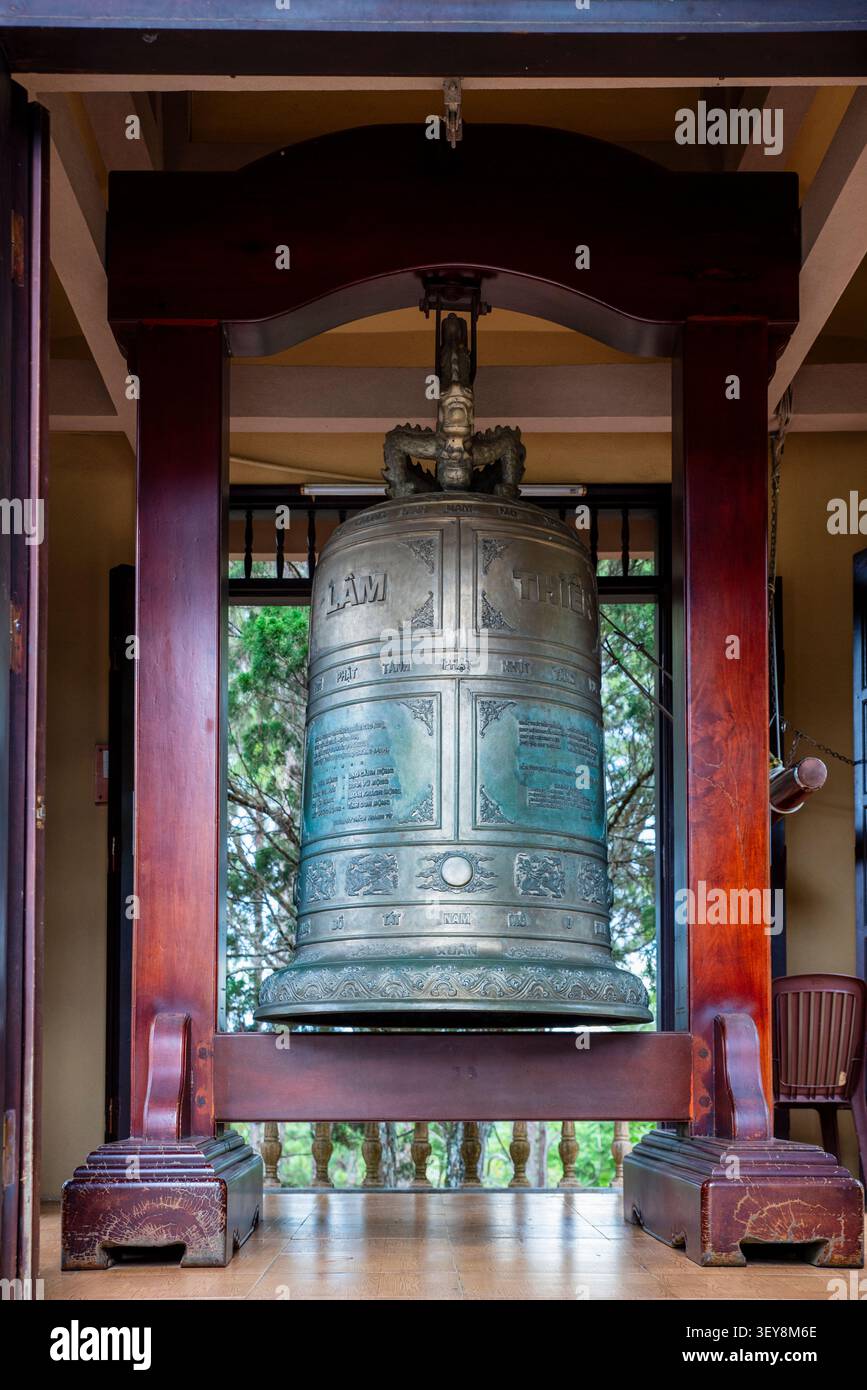 Grande cloche bouddhiste en bronze ornée suspendue dans un cadre en bois dans un temple vietnamien avec des décorations de dragon et des inscriptions gravées dans la tradition Banque D'Images