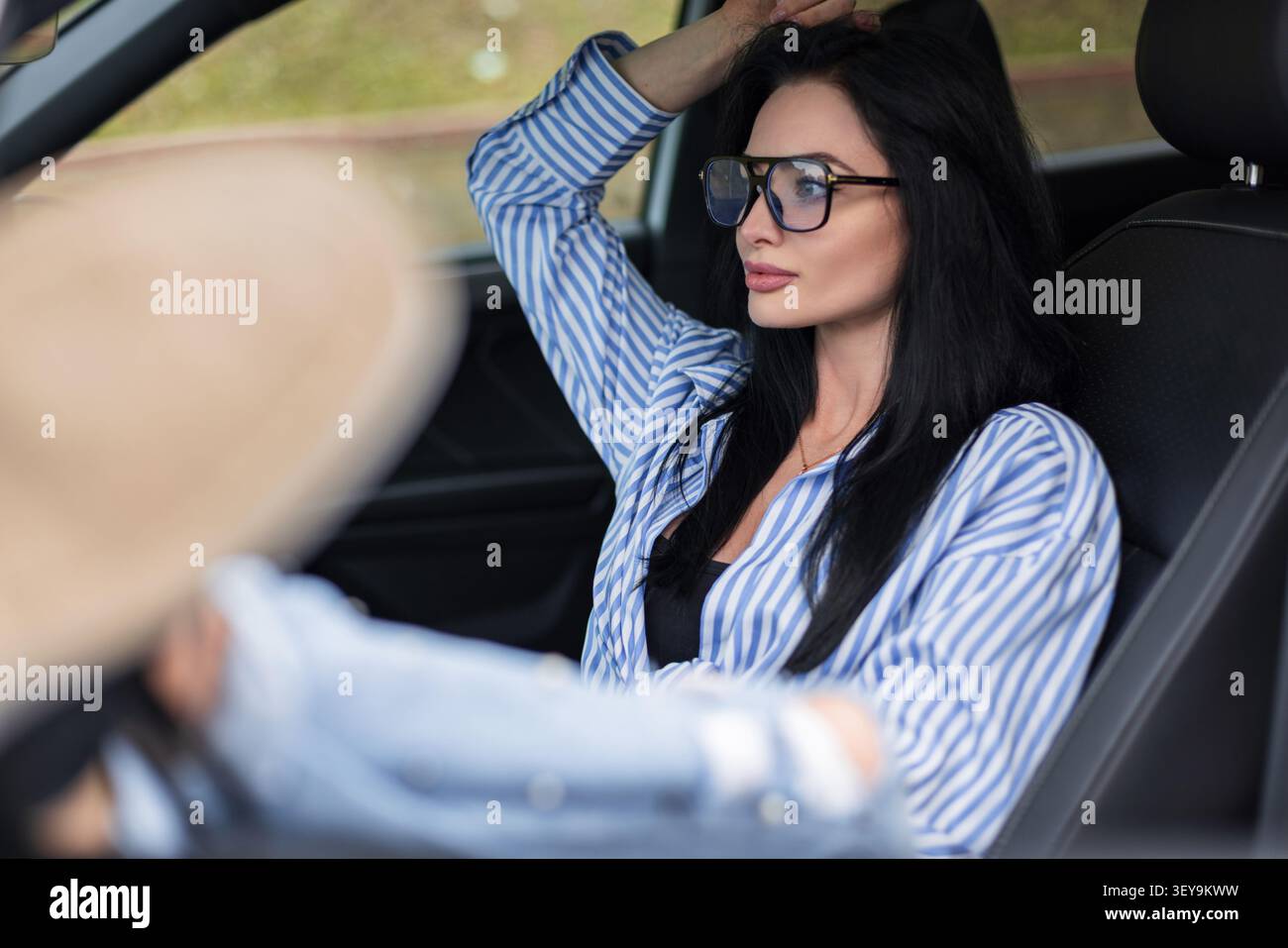 Belle femme millénaire prenant une pause confortable pendant un voyage sur la route, assise dans une voiture avec des sièges en cuir, les pieds vers le haut, regardant loin. Décontracté été l Banque D'Images