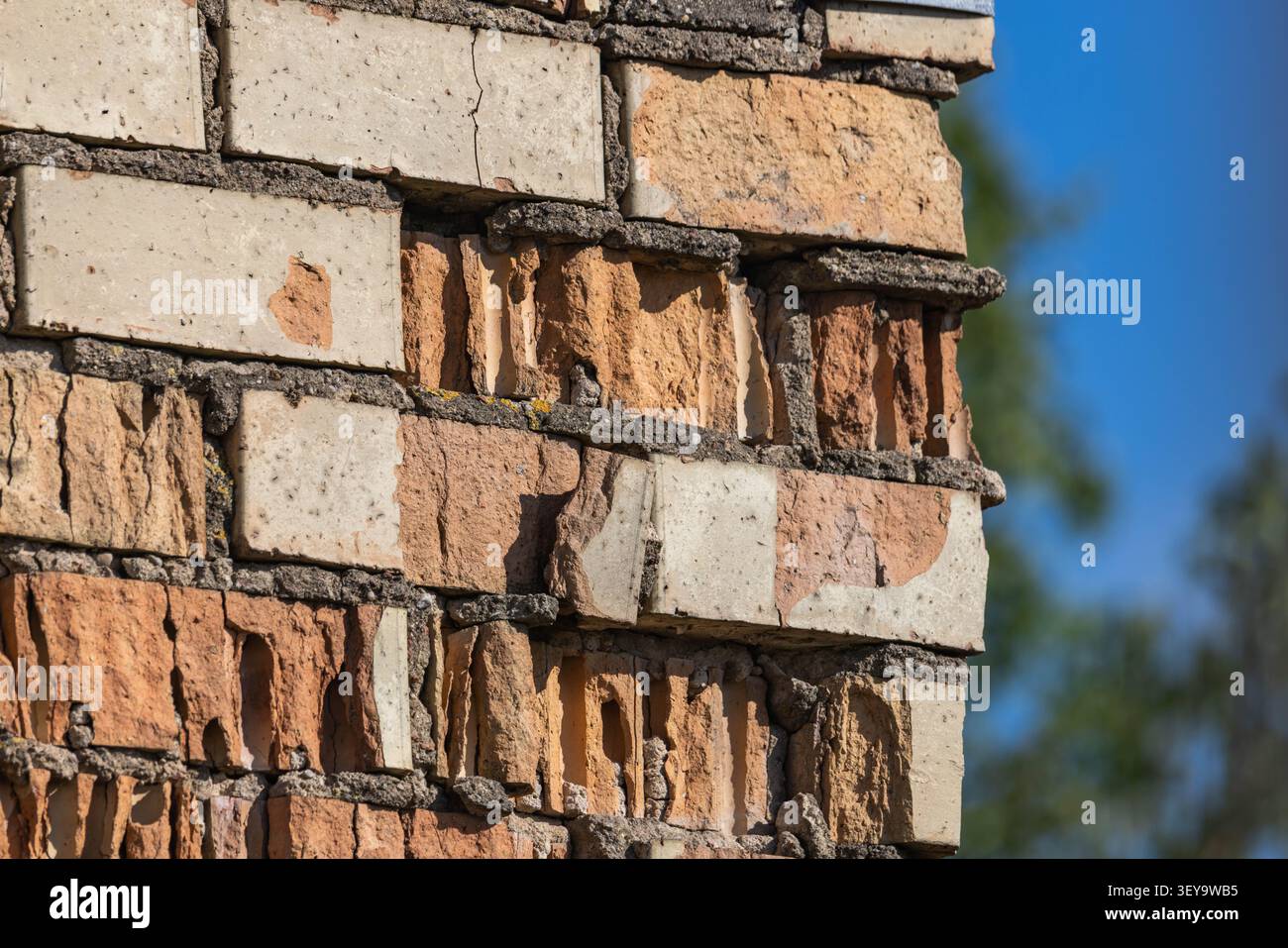 Vue détaillée d'un vieux mur de briques détérioré avec de la maçonnerie fissurée, du mortier endommagé et des briques creuses exposées sous la lumière du jour à l'extérieur. Banque D'Images