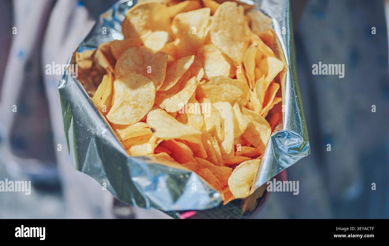 Femme atteignant dans un sac de chips de pomme de terre croustillant, appréciant une collation salée et croustillante avec une texture dorée tentante et un craquelé appétissant Banque D'Images