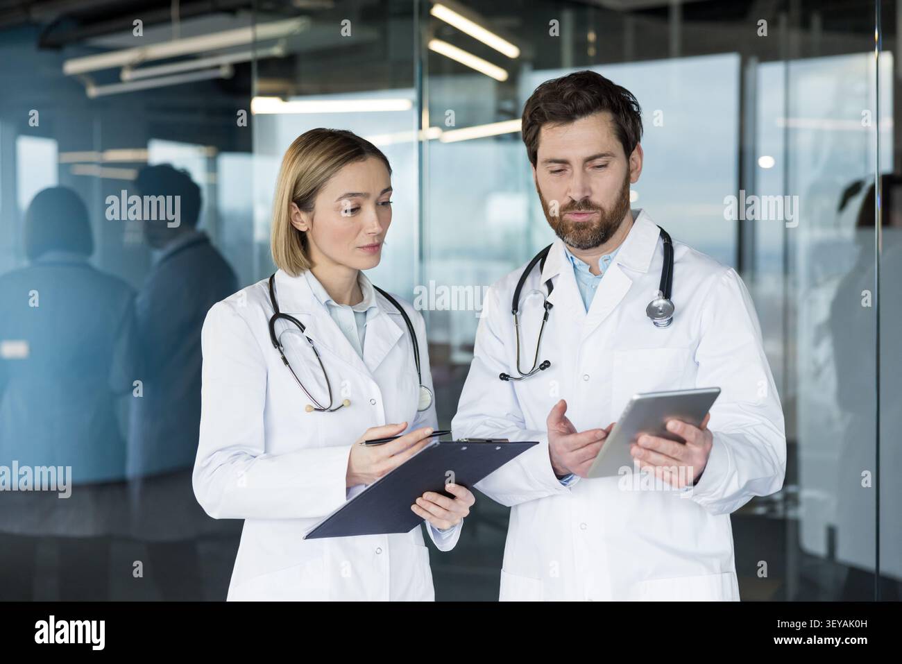 Deux professionnels de la santé collaborent et examinent les informations patient sur une tablette numérique et un presse-papiers physique dans un environnement de bureau moderne Banque D'Images