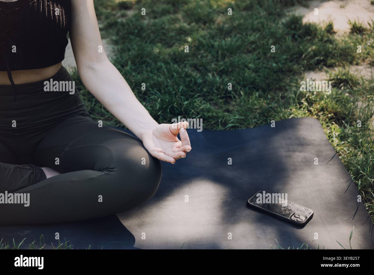 La femme est assise dans la posture de méditation sur le tapis à l'extérieur sur l'herbe. Mode de vie détox numérique, déconnexion de la technologie, réduction consciente du temps d'écran Banque D'Images