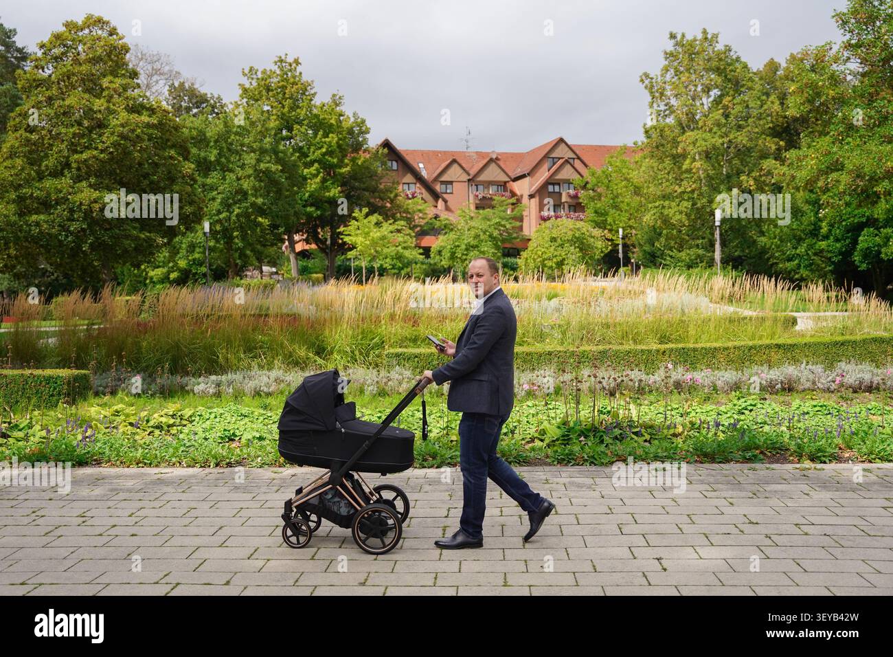 papa d'affaires vêtu d'un costume d'affaires tenant un téléphone dans une main dans l'autre poussant une poussette de bébé noir dans la journée lumineuse d'automne dans le parc Banque D'Images